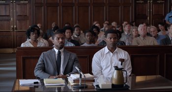 Movie still from “Just Mercy” (2019), directed by Destin Daniel Cretton – Two men sit in front of a crowd in a courtroom; Medium shot, High angle
