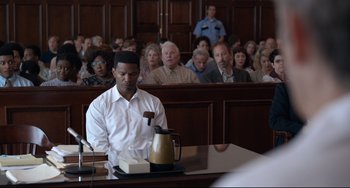 Movie still from “Just Mercy” (2019), directed by Destin Daniel Cretton – A man sitting in front of a crowd in a courtroom; Medium shot, Over the shoulder angle