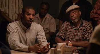 Movie still from “Just Mercy” (2019), directed by Destin Daniel Cretton – A group of men sitting at a table in a room; Medium shot, Over the shoulder angle