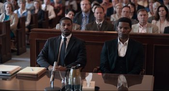 Movie still from “Just Mercy” (2019), directed by Destin Daniel Cretton – Two men in suits sitting at a table in front of a crowd; Medium shot, High angle