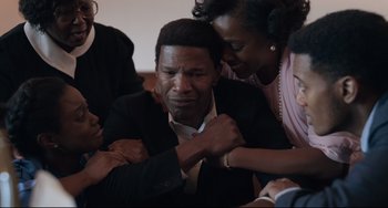Movie still from “Just Mercy” (2019), directed by Destin Daniel Cretton – A group of people gathered around an older man; Medium shot, High angle