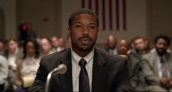 Movie still from “Just Mercy” (2019), directed by Destin Daniel Cretton – A man wearing a suit and tie in front of a microphone; Close Up shot, High angle