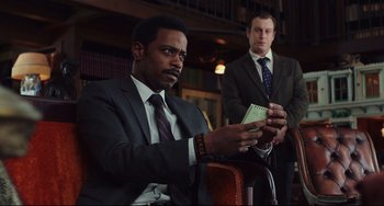 Movie still from “Knives Out” (2019), directed by Rian Johnson – Two men in suits and ties sitting in front of a book; Medium shot, Low angle