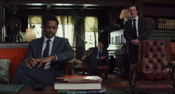 Movie still from “Knives Out” (2019), directed by Rian Johnson – A man in a suit and tie sitting in front of a table; Medium shot, Low angle