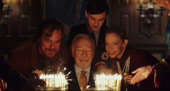 Movie still from “Knives Out” (2019), directed by Rian Johnson – A group of people standing around a table with lit candles on it; Medium shot, Over the shoulder angle