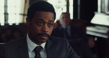 Movie still from “Knives Out” (2019), directed by Rian Johnson – A man in a suit and tie sitting in a room; Close Up shot, Over the shoulder angle