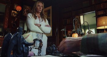 Movie still from “Knives Out” (2019), directed by Rian Johnson – A woman standing in front of a table with books on top of it; Medium shot, Over the shoulder angle