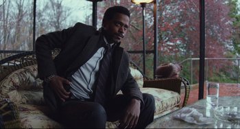 Movie still from “Knives Out” (2019), directed by Rian Johnson – A man sitting on a couch wearing a suit and tie; Medium shot, Low angle