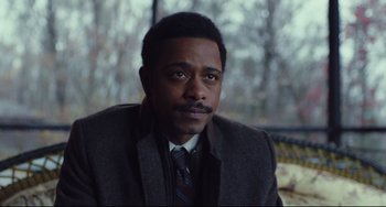 Movie still from “Knives Out” (2019), directed by Rian Johnson – A man in a suit and tie sitting in front of trees; Close Up shot, Over the shoulder angle