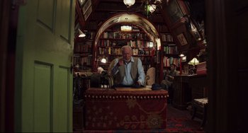Movie still from “Knives Out” (2019), directed by Rian Johnson – An older man sitting in a chair in front of a bookcase; Wide shot, Low angle