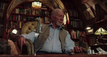 Movie still from “Knives Out” (2019), directed by Rian Johnson – An older man sitting at a table in a library; Medium shot, Low angle