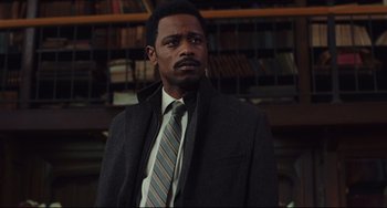 Movie still from “Knives Out” (2019), directed by Rian Johnson – A man wearing a suit and tie standing in front of a bookshelf; Close Up shot, Low angle