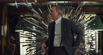 Movie still from “Knives Out” (2019), directed by Rian Johnson – A man in a suit standing in front of a bunch of knives; Medium shot, Low angle
