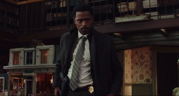 Movie still from “Knives Out” (2019), directed by Rian Johnson – A man in a suit and tie holding a gun in his hand; Medium shot, Low angle