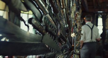 Movie still from “Knives Out” (2019), directed by Rian Johnson – A man is standing in front of a wall of guns; Medium shot, Low angle