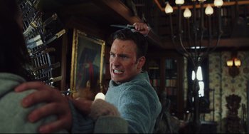 Movie still from “Knives Out” (2019), directed by Rian Johnson – A man is holding a pair of scissors on his head; Medium shot, Over the shoulder angle