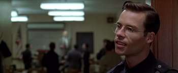 Movie still from “L.A. Confidential” (1997), directed by Curtis Hanson – A man wearing glasses in front of a group of people in a room; Close Up shot, Over the shoulder angle