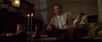 Movie still from “L.A. Confidential” (1997), directed by Curtis Hanson – A man sitting in front of a lit candle and a wine glass; Medium shot, Low angle