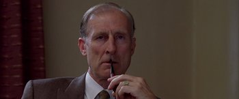 Movie still from “L.A. Confidential” (1997), directed by Curtis Hanson – An older man wearing a suit and tie holding a pipe in his mouth; Close Up shot, Low angle