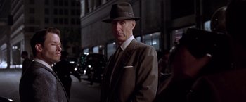 Movie still from “L.A. Confidential” (1997), directed by Curtis Hanson – A man in a suit and hat standing on the street; Close Up shot, Over the shoulder angle