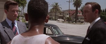 Movie still from “L.A. Confidential” (1997), directed by Curtis Hanson – A man is driving a car down the street; Close Up shot, Over the shoulder angle