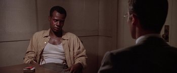 Movie still from “L.A. Confidential” (1997), directed by Curtis Hanson – A man in a plaid shirt is sitting in a room; Medium shot, Over the shoulder angle