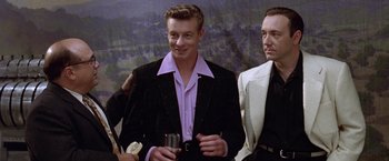 Movie still from “L.A. Confidential” (1997), directed by Curtis Hanson – A man holding a wine glass in front of two other men; Medium shot, Over the shoulder angle