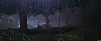 Movie still from “L.A. Confidential” (1997), directed by Curtis Hanson – A man sitting on the hood of a car in the rain; Extreme Wide shot, High angle