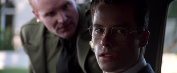 Movie still from “L.A. Confidential” (1997), directed by Curtis Hanson – A man with glasses is looking at the camera while another man looks at the camera; Close Up shot, Over the shoulder angle