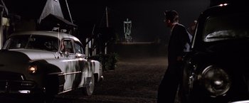 Movie still from “L.A. Confidential” (1997), directed by Curtis Hanson – A man standing next to an old car in the dark; Wide shot, Low angle