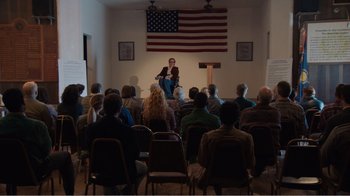 Movie still from “Don't Worry, He Won't Get Far on Foot” (2018), directed by Gus Van Sant – A group of people sitting in front of an american flag; Wide shot, High angle