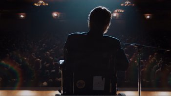 Movie still from “Don't Worry, He Won't Get Far on Foot” (2018), directed by Gus Van Sant – A man sitting in a chair in front of a microphone; Wide shot, High angle