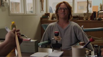 Movie still from “Don't Worry, He Won't Get Far on Foot” (2018), directed by Gus Van Sant – A man sitting at a table holding a cell phone; Medium shot, Over the shoulder angle