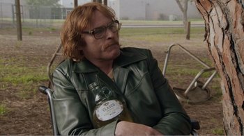 Movie still from “Don't Worry, He Won't Get Far on Foot” (2018), directed by Gus Van Sant – A man sitting on a park bench holding a bottle of alcohol; Medium shot, Over the shoulder angle