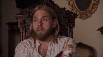 Movie still from “Don't Worry, He Won't Get Far on Foot” (2018), directed by Gus Van Sant – A man with long hair and beard sitting in front of a wooden chair; Close Up shot, High angle