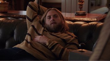 Movie still from “Don't Worry, He Won't Get Far on Foot” (2018), directed by Gus Van Sant – A man with long hair and beard sitting on a couch with his arms crossed; Medium shot, High angle