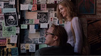Movie still from “Don't Worry, He Won't Get Far on Foot” (2018), directed by Gus Van Sant – A man and a woman sitting next to each other in front of a wall covered with stickers; Medium shot, Over the shoulder angle