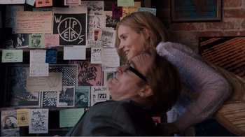 Movie still from “Don't Worry, He Won't Get Far on Foot” (2018), directed by Gus Van Sant – A man and a woman sitting next to each other in front of a wall covered in stickers; Medium shot, Over the shoulder angle