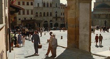 Movie still from “Life Is Beautiful” (1997), directed by Roberto Benigni – Two women walking down the street with a horse drawn carriage in the background; Extreme Wide shot, High angle