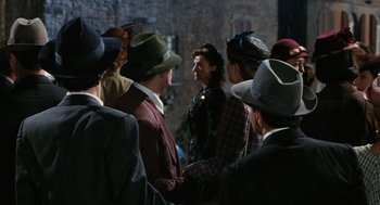 Movie still from “Life Is Beautiful” (1997), directed by Roberto Benigni – A group of people standing around a building wearing hats; Medium shot, Over the shoulder angle