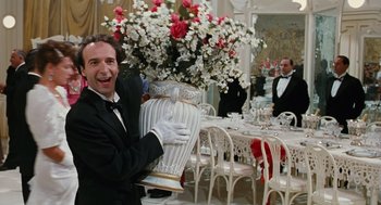 Movie still from “Life Is Beautiful” (1997), directed by Roberto Benigni – A man in a tuxedo holding a vase in front of a dining room table; Medium shot, Low angle