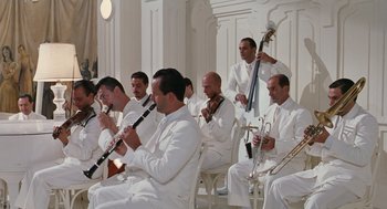 Movie still from “Life Is Beautiful” (1997), directed by Roberto Benigni – A group of men in white suits playing musical instruments; Wide shot, Low angle