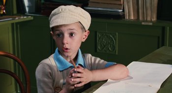 Movie still from “Life Is Beautiful” (1997), directed by Roberto Benigni – A young boy wearing a hat is sitting at a table; Close Up shot, High angle
