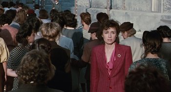 Movie still from “Life Is Beautiful” (1997), directed by Roberto Benigni – A woman in a red suit standing in front of a group of people; Medium shot, High angle