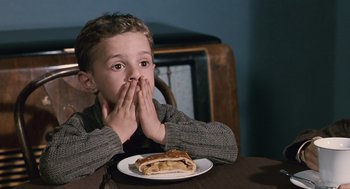 Movie still from “Life Is Beautiful” (1997), directed by Roberto Benigni – A young boy sitting at a table with a sandwich in front of his face; Close Up shot, Over the shoulder angle