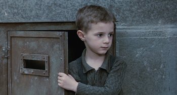 Movie still from “Life Is Beautiful” (1997), directed by Roberto Benigni – A young boy standing in front of an open door; Medium shot, Low angle
