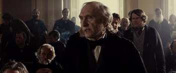 Movie still from “Lincoln” (2012), directed by Steven Spielberg – An old man in a suit and bow tie in front of a group of people; Close Up shot, Over the shoulder angle