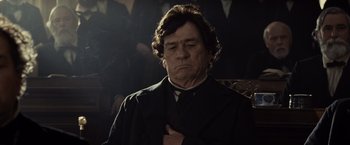 Movie still from “Lincoln” (2012), directed by Steven Spielberg – An old man in a black suit is holding his hands to his chest; Close Up shot, Low angle