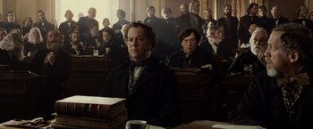 Movie still from “Lincoln” (2012), directed by Steven Spielberg – A man sitting in front of a group of people in a courtroom; Medium shot, Low angle