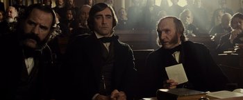 Movie still from “Lincoln” (2012), directed by Steven Spielberg – Two men sitting at a table in front of a crowd; Medium shot, Low angle